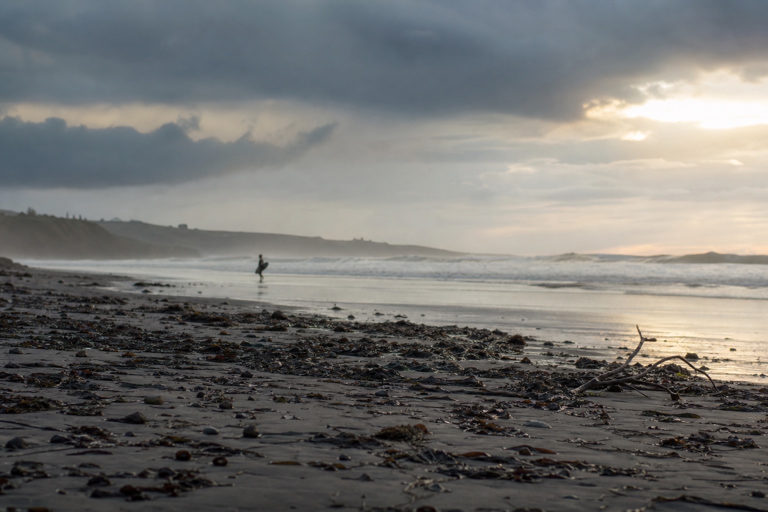 Plage normande après une tempête hivernale : houle résiduelle, ciel délavé et silhouette lointaine de surfeur